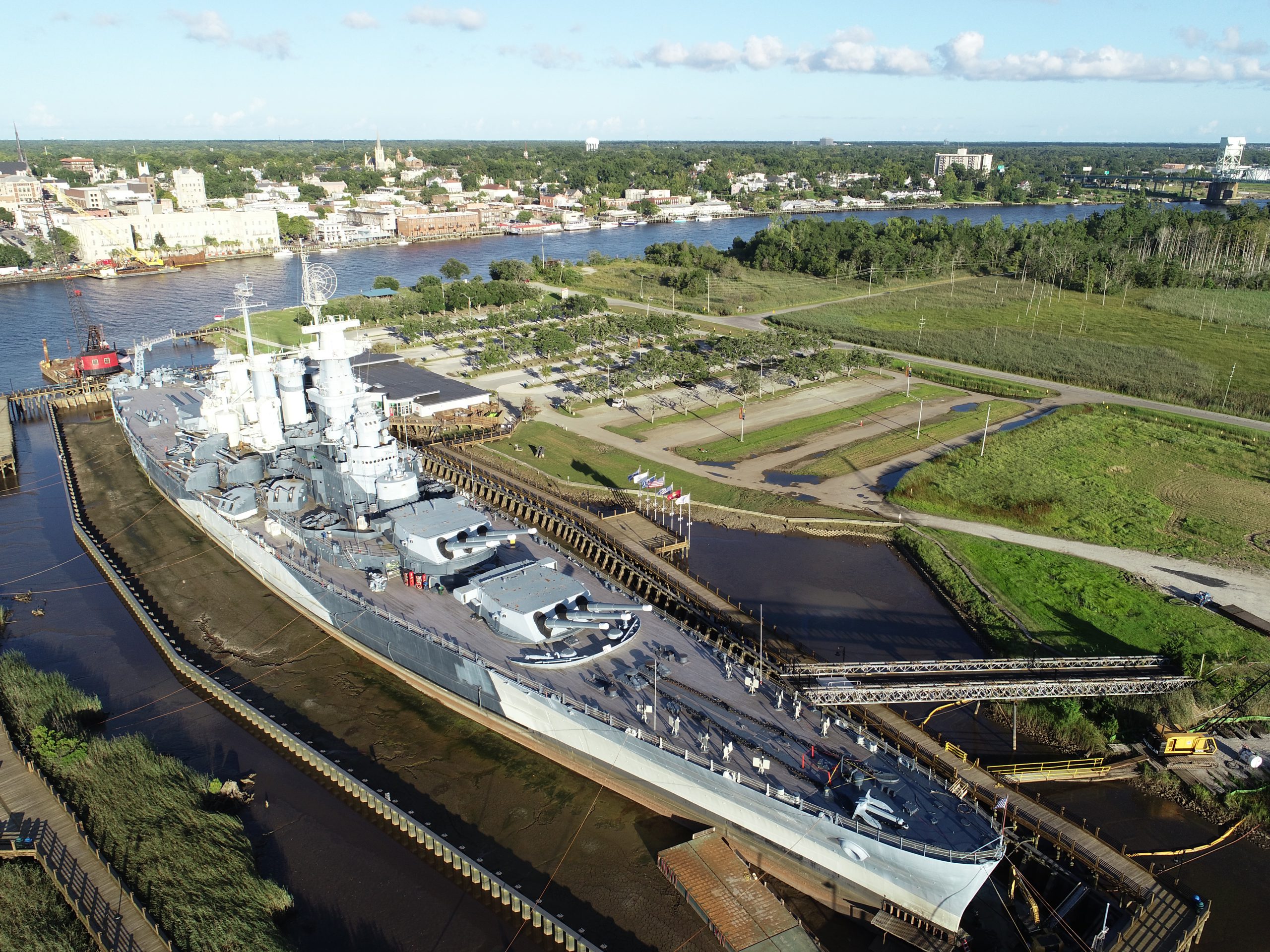 Aerial view of a stationary battleship (USS North Carolina) on a river with an adjacent parking lot