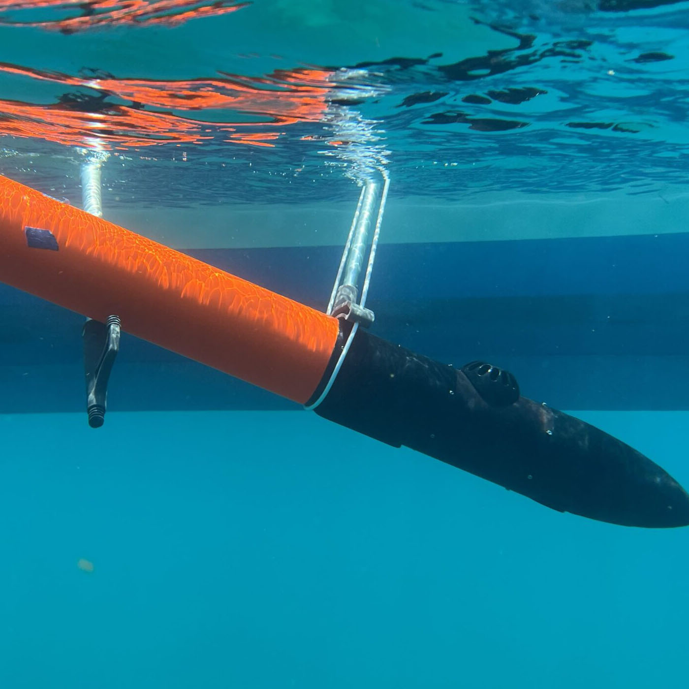 And underwater view of a black and orange torpedo like object being lowered into the water.