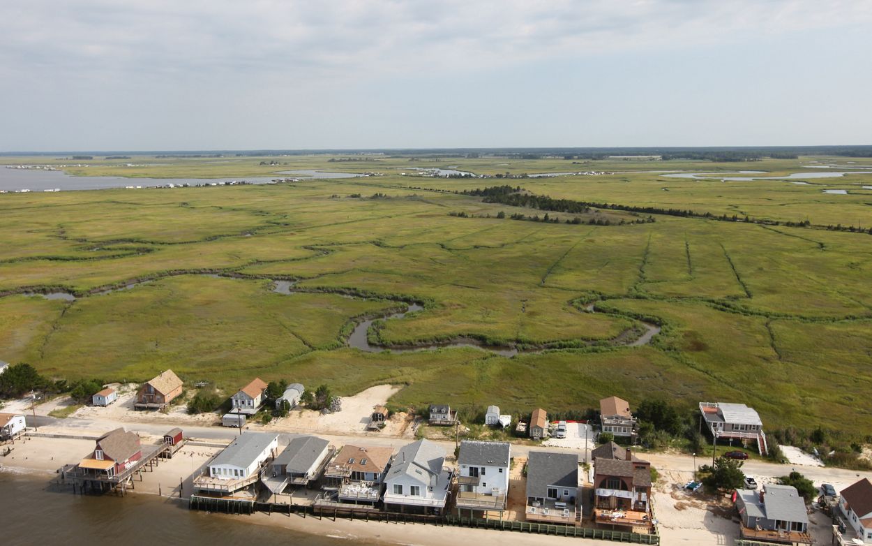 A line of houses on an eroded beach with a vast marsh in the background.