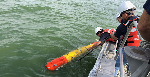Three people on a boat lower an autonomous underwater vehicle into the water.