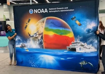 Two people stand on either side of a large, NOAA banner.