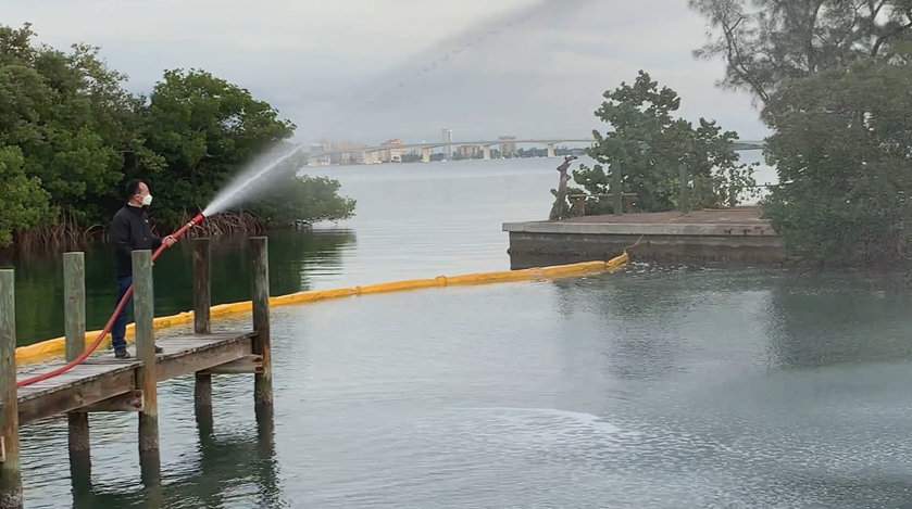 Man on a dock sprays a substance into a body of water.