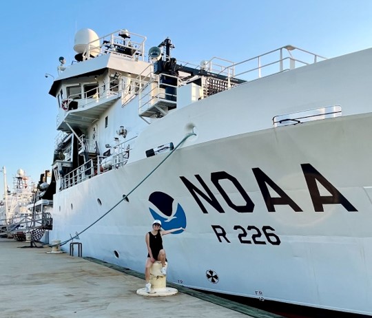 Claire Huang sitting on a dock next to a large NOAA ship