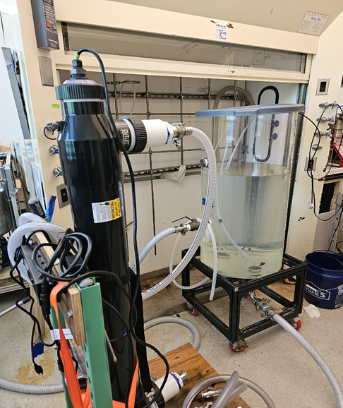 Laboratory setting showing large, cylindrical tank of water connected to hoses that deliver nanobubble ozone to remove harmful PFAS chemicals from water.