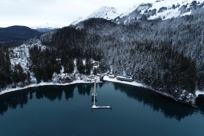 a dock in a lake surrounded by snowy mountains and trees.
