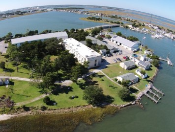 Aerial view of a facility with multiple buildings, docks, and a parking lot. Water surrounds the grounds
