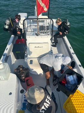 overhead image of four people in a boat; two divers prepare to enter the water while the other two prepare water samples