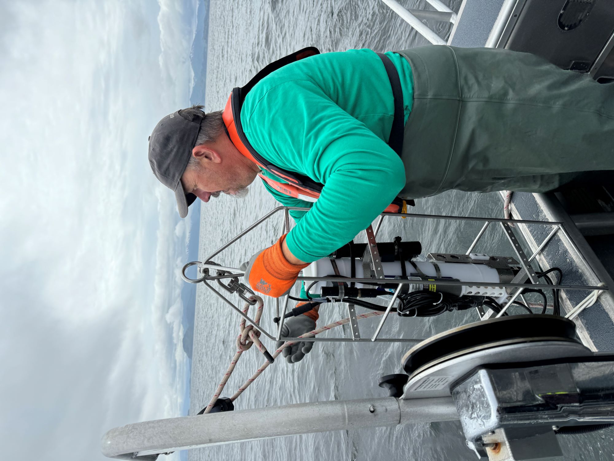 Woman deploys CTD over back of research vessel, sunset is visible in the background