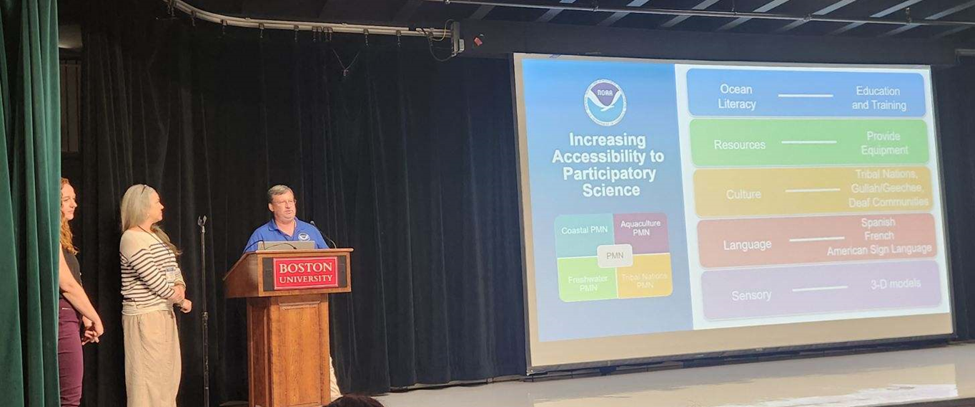 Three people stand on stage with a presentation titled Increasing Accessibility to Participatory Science