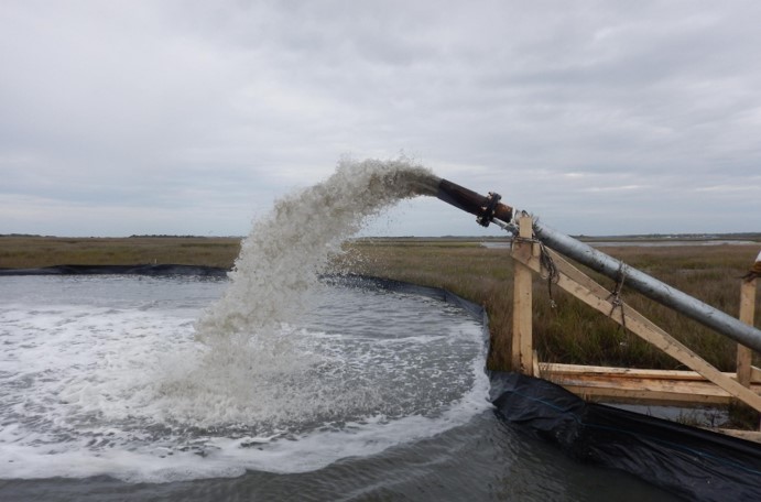 pipe shoots sandy water into a designated marsh area.