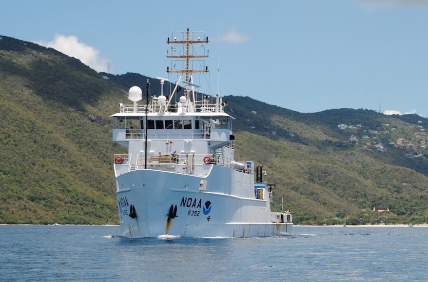 A NOAA ship cruises along a mountainous shoreline.