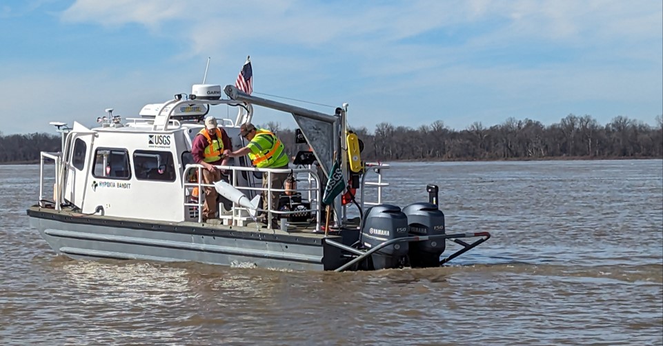 Two people on a boat pulling an unoccupied underwater vehicle from the water.