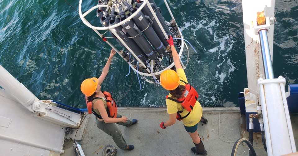 two people on a boat reach for an instrument suspended over the water