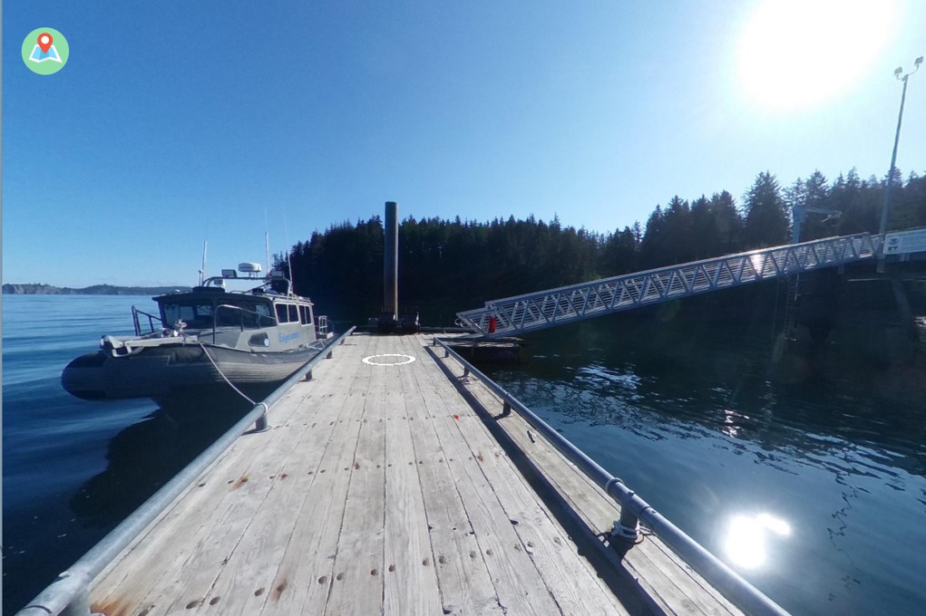 View from a dock with boat on the left and ramp on the right. A circle is in the center of the dock and map icon is in the upper left corner of the image.