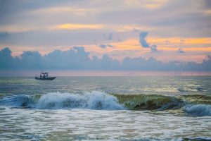 boat at sunset, waves crashing in the foreground 