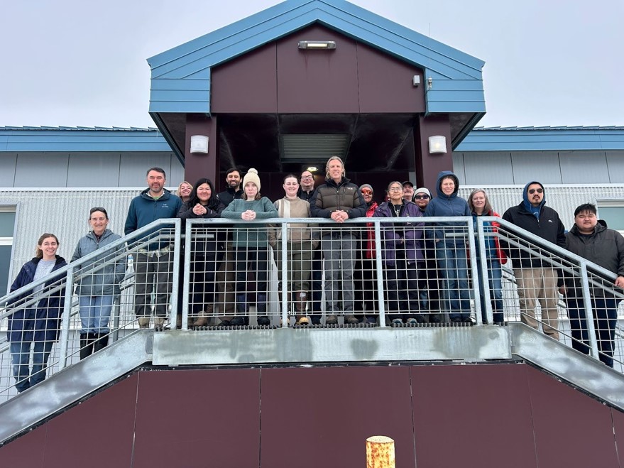 A group of people (workshop attendees) stand on the porch of a building