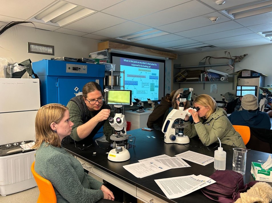 Man adjusts microscope as others view into other microscopes.