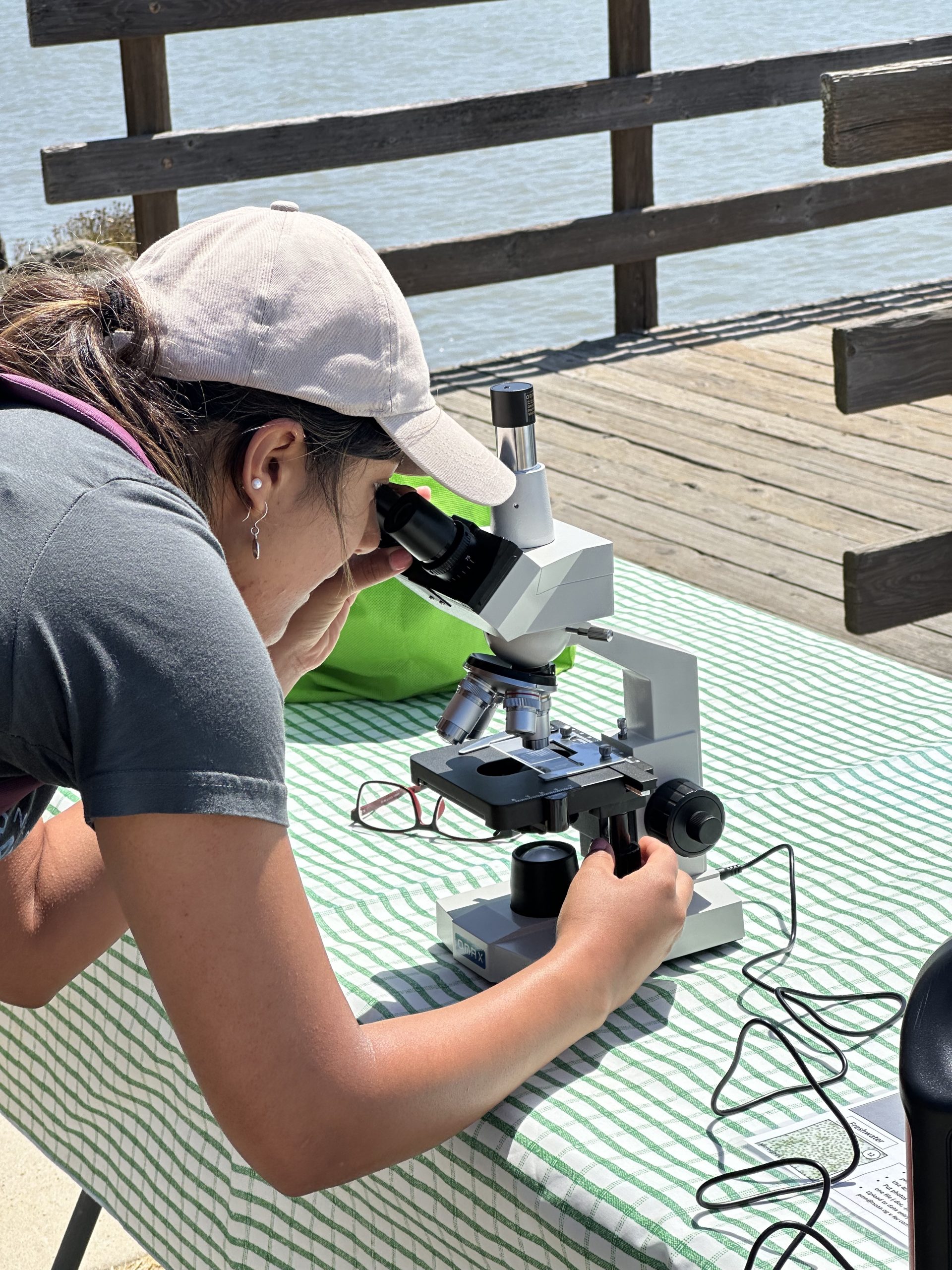 Woman on a waterfront dock looks through a microscope to identify phytoplankton.