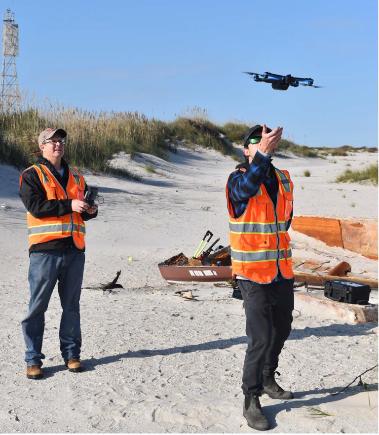 two men on a beach fly a drone