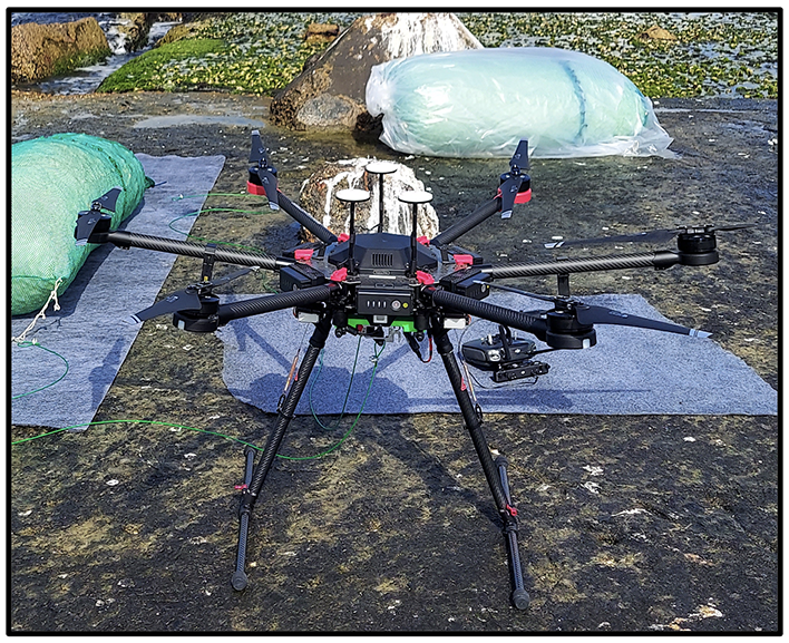 Unmanned aircraft system drone preparing for measurements near Galveston Bay, Texas, with bags of tracer particles (biodegradable packaging peanuts) in the background.